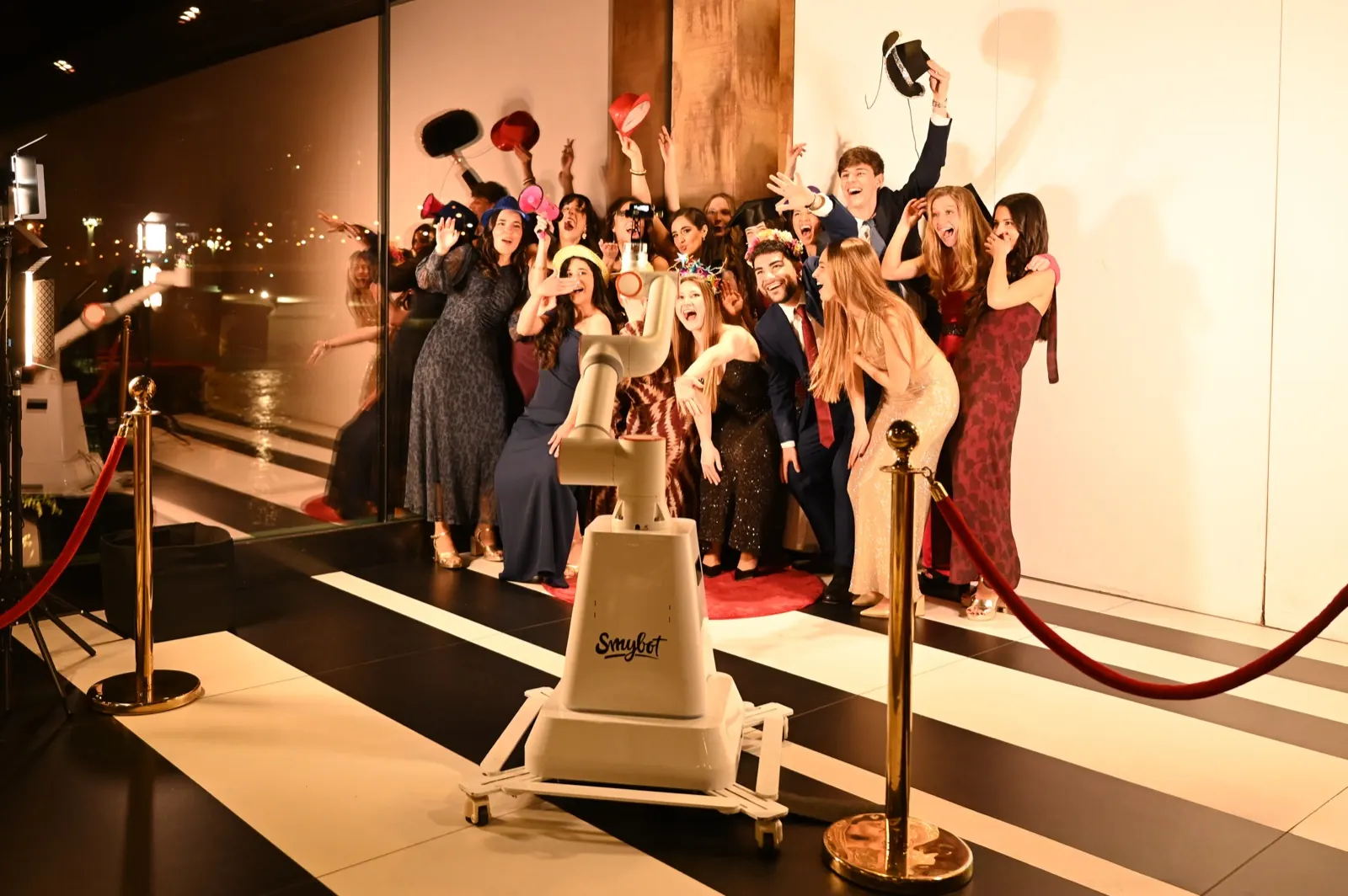 Graduados celebrando detrás del Glambot Smybot en la alfombra roja